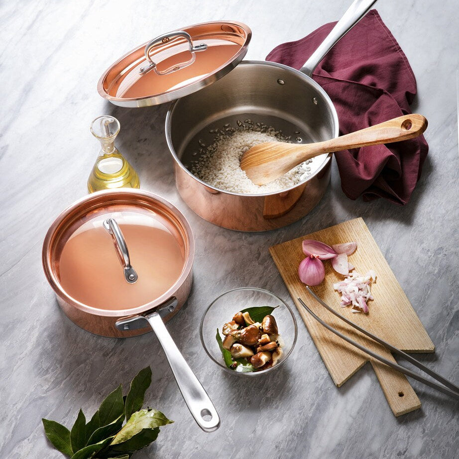 Copper cookware set with a wooden spoon and ingredients on a gray surface